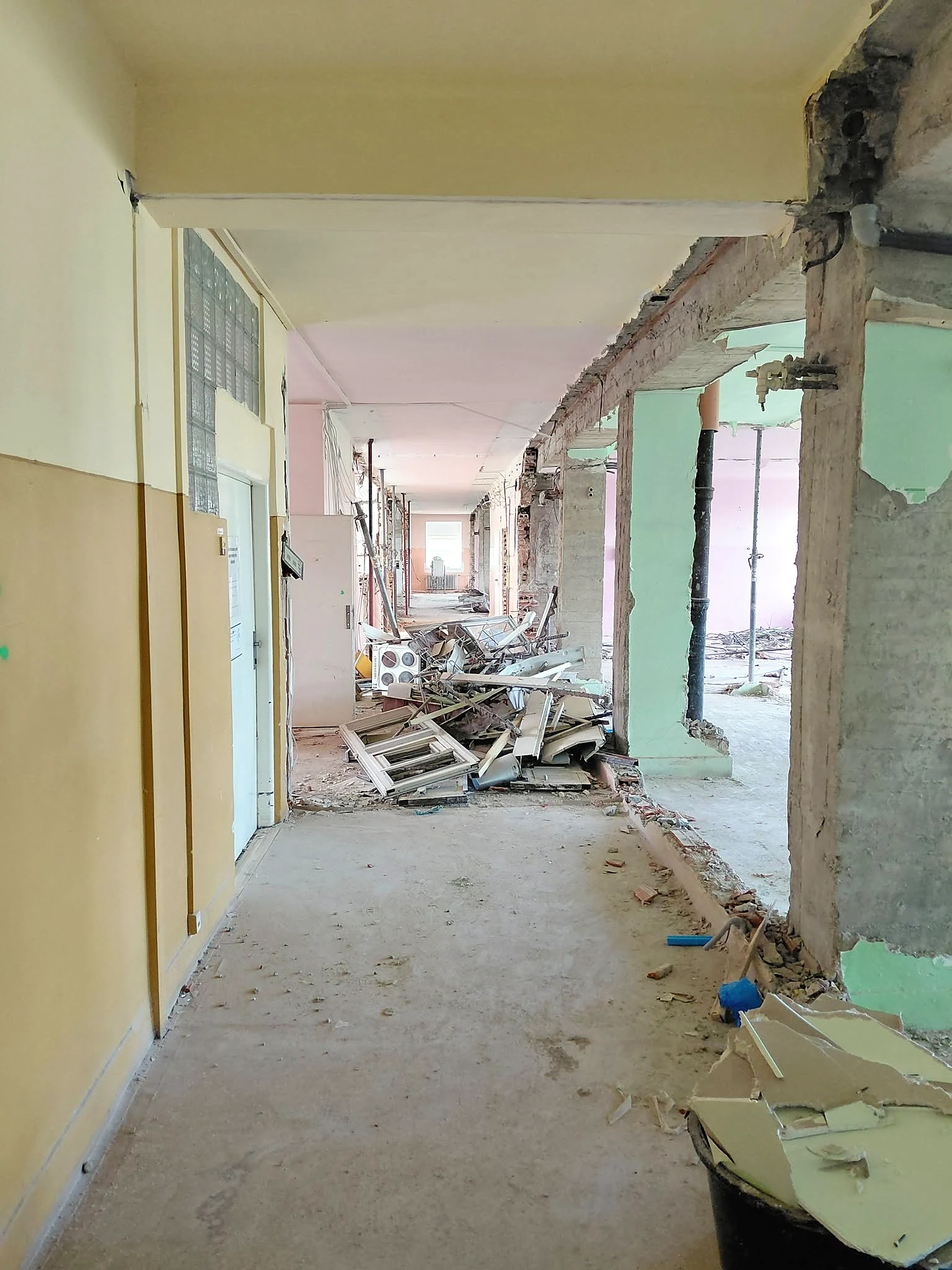 Korytarz przed remontem — stare lamperie, wyburzone ścianki, gruz ze starych ościeżnic i stalowe stemple pod stropem