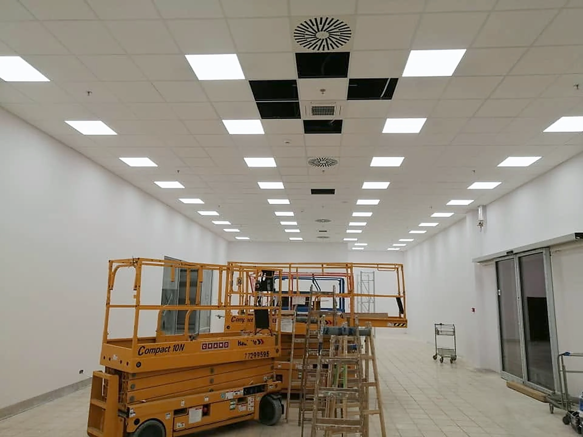 Sala sprzedaży z gotowym sufitem kasetonowym i panelami LED; na środku stoi podnośnik nożycowy